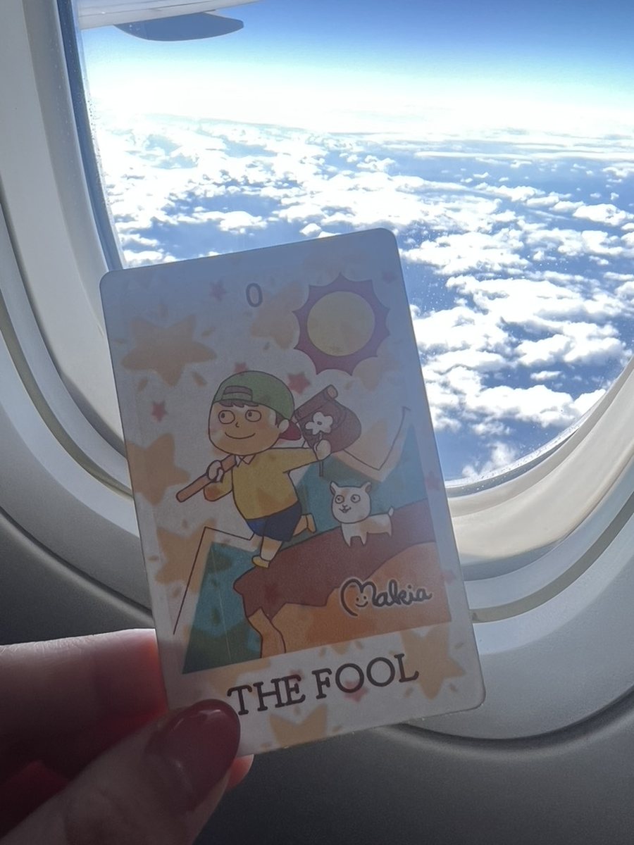 飛行機の窓辺で手づくりの愚者のカードを持っているところ